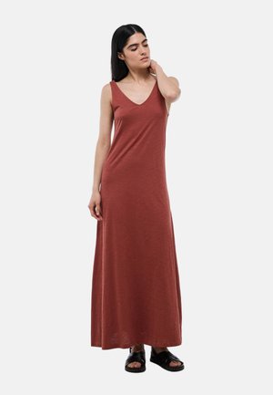 Robe maxi de couleur rouille, en tissu doux. Elle présente un décolleté en V, sans manches et une coupe ample, atteignant les chevilles. Sandales noires portées.