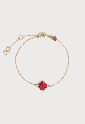 Delicada pulsera de cadena de oro con un charm de trébol de cuatro hojas rojo en el centro y un pequeño charm de corazón cerca del cierre con longitud ajustable.