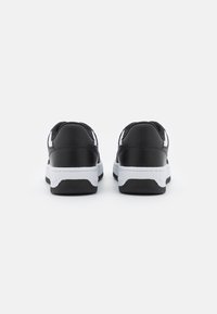 Sneakers neri con accenti bianchi, tomaia sintetica liscia, colletto imbottito e suola piatta in gomma. Design minimalista, vista posteriore.