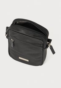 Sort nylon crossbody taske med lynlås, slank rektangulær form, frontlomme og logo-plade i sølvfarve. Justerbar rem medfølger.