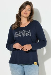 Maglia a maniche lunghe blu navy con grafica di un cane chiaro sul davanti, dettaglio con cerniera laterale e una vistosa toppa del logo gialla all'orlo.
