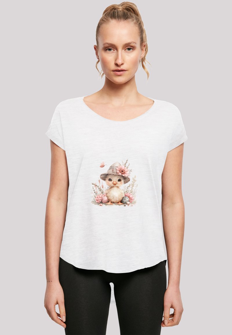Weißes T-Shirt mit kurzen Ärmeln, das eine bedruckte Illustration eines Vogels mit einem Hut und Blumen zeigt, akzentuiert durch sanfte Rosatöne und natürliche Elemente.