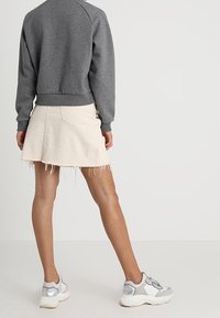 Felpa grigia con orlo a coste, gonna di jeans crema con bordi sfrangiati e sneaker bianche con dettagli in argento. Focus sugli abiti casual.