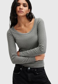 Maglietta grigia a maniche lunghe in tessuto a costine con scollatura ampia, abbinata a jeans scuri. Presenta maniche aderenti e una silhouette slim.