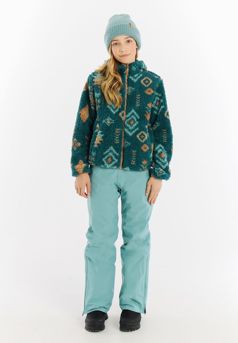 Giacca in pile teal con motivi geometrici, con zip frontale e tasche con zip; abbinata a pantaloni impermeabili teal chiaro e stivali da neve neri.