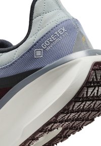 Sneaker bleu clair et gris avec une tige en tissu texturé, marquage GORE-TEX, et une semelle blanche rembourrée avec un motif en caoutchouc noir.