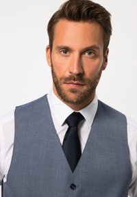 Gilet azzurro su misura con una finitura texture, indossato sopra una camicia bianca e abbinato a una cravatta scura.