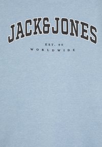 Sudadera azul claro con "JACK&JONES" en letras negras en arcos en negrita, texto adicional "EST. 90" y "WORLDWIDE" en fuente negra más pequeña debajo.