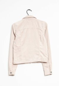 Vaaleanbeige corduroy-takki roikkuu mustassa niskassa, taka näkymä, pitkät hihat napillisilla hihansuilla, kaulus taitettuna alas.