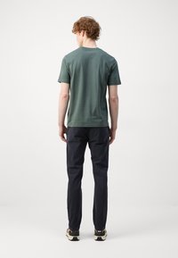 T-shirt en coton vert à col rond et manches courtes, associé à un pantalon bleu marine foncé et des baskets. Design uni sans logos ni motifs visibles.