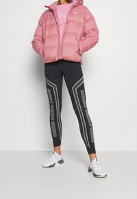 Różowa kurtka z ociepleniem i kapturem, elastyczne mankiety; czarne legginsy z odblaskowymi szarymi paskami i napisem; białe trampki z czarnymi plamkami na podeszwie.