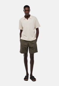 Polo beige à manches courtes avec un col, associé à un short vert olive et des sandales noires avec une semelle texturée.