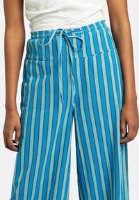 Blå randiga vida byxor med dragsko i midjan. Ränderna har nyanser av blått och grått. Mjuk textur med sidfickor.