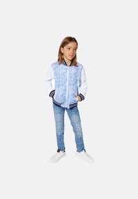 Blauwe en witte bomberjack met logo patroon, geribde kraag en manchetten, gecombineerd met blauwe jeans met logo-print en witte sneakers.