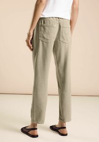 Pantalones de color verde oliva claro con un corte holgado, que cuentan con dos bolsillos traseros y una cómoda cinturilla elástica, combinados con sandalias de malla negras.