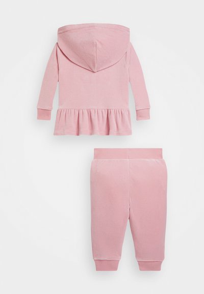 Ružový velúrový teplákový komplet s kapucňou a peplum lemom, spolu s nohavicami so zúženými manžetami. Mäkká textúra po celom úseku.