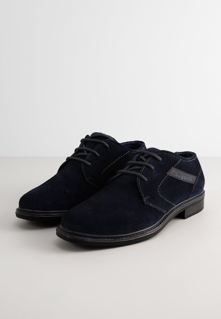 Marineblauwe suede leren schoenen met een soepele afwerking, voorzien van grijze veters, een contrasterend gestikt ontwerp en een subtiele logo-accent aan de zijkant.