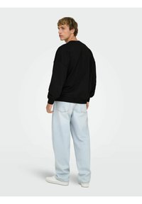 Felpa nera oversize con spalle scese, polsini e orlo a costine, abbinata a jeans larghi azzurri chiari e sneakers bianche.