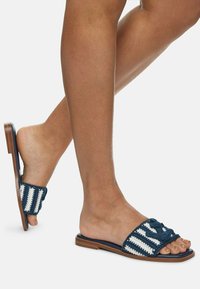 Sandali scivolati intrecciati a righe blu e bianche con suola piatta marrone, caratterizzati da un design con cinturini intrecciati e retro aperto. Tessuto resistente.