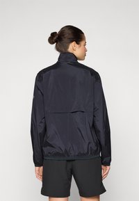 Zwarte lichtgewicht jas met opstaande kraag, ritszak aan de achterkant en elastische manchetten. Glad textuur en een relaxte pasvorm ontworpen voor comfort.