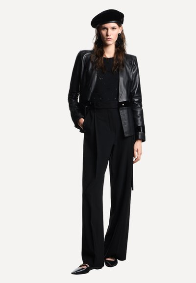 Giacca in pelle nera con silhouette aderente, abbinata a pantaloni neri a vita alta. Accessori comprendono un basco nero e ballerine con punta affusolata.