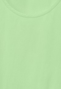 Tessuto verde chiaro con una texture liscia e un collo rotondo. Il materiale sembra morbido e leggermente elasticizzato. Nessun motivo o decorazione visibile.