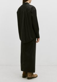 Schwarzes langärmliges Shirt mit abgerundetem Saum, kombiniert mit einem langen Rock aus dunklem Denim und braunen Ankle Boots mit Schnürdetails.