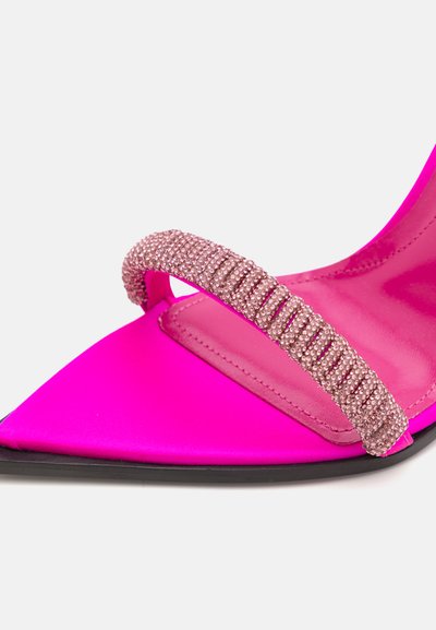 Zapato de stiletto de satén rosa con punta afilada; cuenta con una correa de pedrería brillante a lo largo de la parte superior. Suela negra. Textura suave.