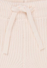 Cremfarbene gestrickte Hose mit einem gerippten Taillenbund und einer gebundenen Kordel. Die Textur ist weich und mit einem gleichmäßigen Muster gewebt.