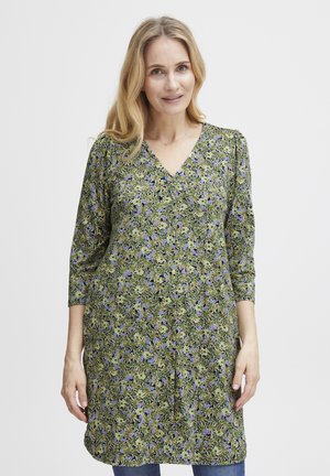Blommig tunikaklänning i grön, med V-ringning, 3/4-långa ärmar och ett mönster av små lila blommor mot en lövbakgrund.