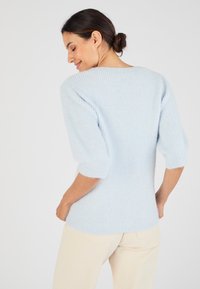 Maglione a costine di un blu chiaro, con maniche a puff 3/4, morbido al tatto, colletto rotondo e una vestibilità allungata, abbinato a pantaloni di colore chiaro.