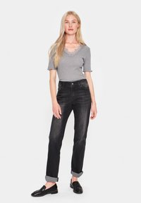 Top grigio a maniche corte con dettagli in pizzo, abbinato a jeans neri a vita alta con risvolti e mocassini neri su uno sfondo neutro.