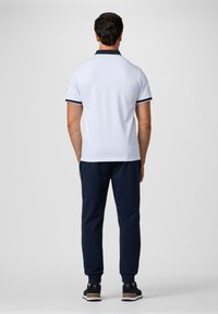 Biely polo tričko s námorníckymi detailmi na golieri a rukávoch, skombinované s tmavo námorníckymi zúženými nohavicami. Topánky majú textúrovaný čierny zvršok a béžovú podrážku.