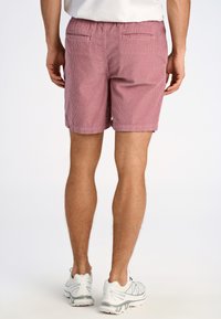 Pantaloni corto a righe rosa con vita elastica, due tasche posteriori e una vestibilità rilassata, abbinati a scarpe da ginnastica bianche.