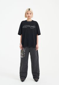 Svart bomull t-shirt med en silvrig broderad "Ed Hardy"-logotyp, matchad med mörka jeans i denim med färgglada ormbitar och dödskallegrafik.