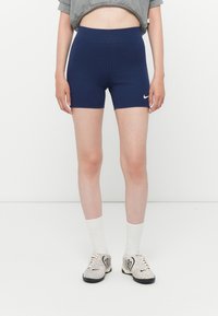 Calças de treino azul marinho com uma cintura alta e textura suave, apresentando um logo da Nike branco na coxa esquerda.