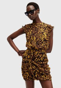 Robe imprimée léopard en jaune et marron avec des manches volantes et une silhouette ajustée, mettant en avant une texture froncée et un design froncé.