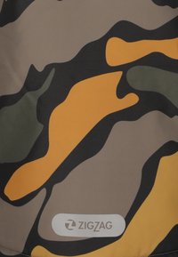 Tarnmusterstoff in Brauntönen, Grüntönen und Orange. Enthält ein weißes Logo mit "ZIGZAG" in einem abgerundeten Rechteck am unteren Rand.
