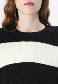 Pulover cu dungi alb-negru, cu o textură ribidă, având un guler rotund. Dungile sunt distribuite uniform pe zona pieptului.