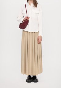 Camicia bianca a maniche lunghe con taschini sul petto, gonna beige plissettata, stivali neri con platform e una piccola borsa a spalla borgogna.
