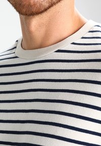 T-shirt en coton à rayures marines avec un col rond côtelé. Le tissu semble doux et léger, présentant des rayures alternées foncées et claires.