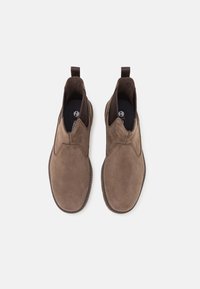 Botine din suede, de culoare maro, cu panouri elastice laterale, vârf rotunjit și talpă din cauciuc texturat. Interiorul dispune de căptușeală moale și un branț cu marcaj.