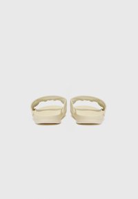 Light beige slide sandals with a textured upper, open toe design, and curved straps. Solid rubber soles provide grip and comfort.