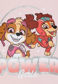 Zwei Cartoon-Hunde sind auf einem pinken Hintergrund zu sehen, mit verspielten Gesichtsausdrücken. Einer trägt ein pinkes Headset, der andere einen roten Anzug. "POWER Girls" in glitzerndem Text darunter.