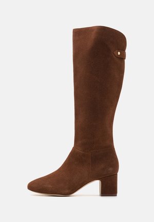Botte haute en daim marron, avec un bout pointu et un talon bloc. Présente une texture lisse et un petit accent métallique près du haut.