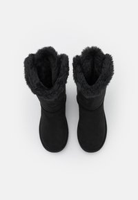 Bottines noires en daim avec une douce doublure en fausse fourrure autour de la cheville. Présentent un extérieur lisse et un design à bout rond.