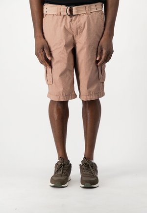 Mann trägt hellbraune Cargoshorts mit einem Stoffgürtel und dunkelbraunen Turnschuhen, steht vor einem schlichten weißen Hintergrund.