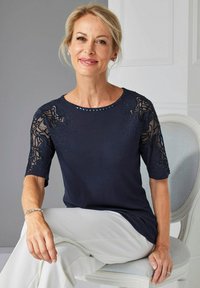 Donkerblauw topje met korte, doorschijnende kant mouwen met bloemmotieven en strassaccenten. Zachte stof met een ontspannen pasvorm.