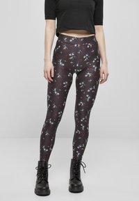 Leggings à motifs floraux en tissu sombre avec une taille haute. Présente des motifs floraux colorés sur un fond noir. Associés à des bottes noires.