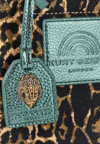 Borsa in tessuto con stampa leopardata beige e nera, dotata di un'etichetta verde menta testurizzata con hardware dorato e un dettaglio logo impresso.